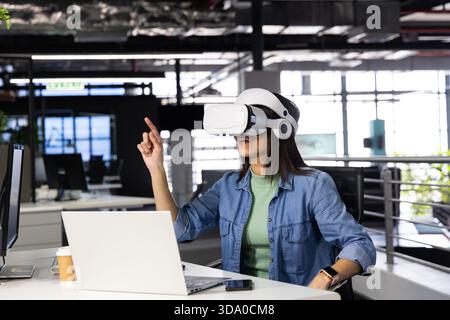 VR headset resting on desk near windows revealing greenery in office, with laptop and coffee cup Stock Photo