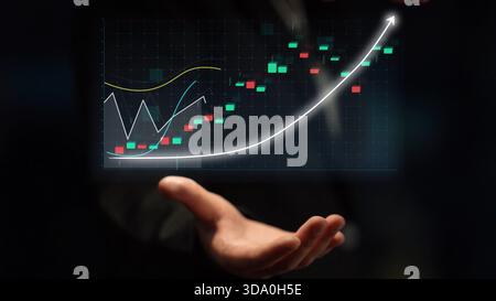 A hand extends towards a digital screen displaying a stock market graph, featuring colorful candlesticks and curves that indicate growth and financial Stock Photo