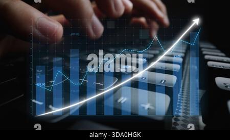 This image captures hands typing on a keyboard with an overlay of a financial growth graph, representing market analysis and business trends in a Stock Photo