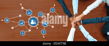 A diverse group of professionals joining hands on a wooden desk with digital icons, showcasing collaboration and technological innovation in a modern Stock Photo