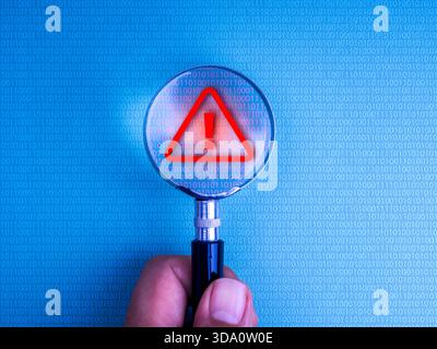 Magnifying glass in hand over binary code on computer screen detecting red warning symbol. Concept of cyber security alert, scam detection, data breac Stock Photo