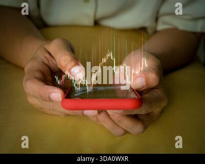 Close-up hands holding smartphone with stock market chart overlay, symbolizing online trading, investment tracking, financial analytics, and modern te Stock Photo