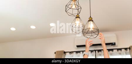 Woman hands reaching for hanging pendant light bulbs in modern home showing interior lighting decoration energy ideas creativity warm atmosphere comfo Stock Photo
