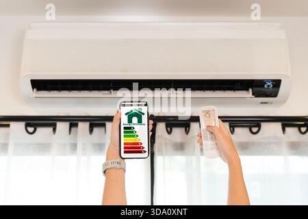 Hands holding smartphone showing energy efficiency and remote controlling air conditioner at home saving electricity cooling smart living technology c Stock Photo