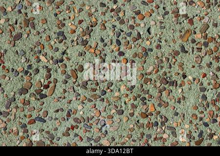 Green concrete surface embedded with small stones pebbles close-up abstract textured background Stock Photo