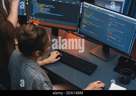 IT developers discussing with point to intelligent website development coder system running data online on pc of two screens with information Stock Photo