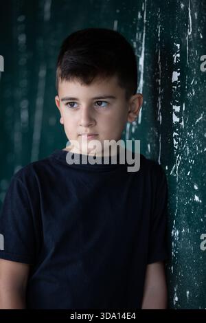 10 years old boy leaning against decayed wall looking away Stock Photo
