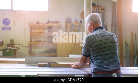 Senior carpenter cutting wood plank using a table saw Stock Photo
