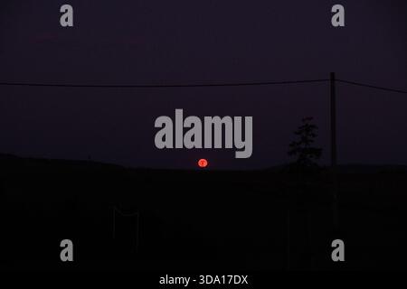 Dramatic night scene featuring a vibrant red moon illuminating a dark, rural landscape. Peaceful and atmospheric. Stock Photo