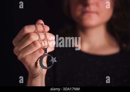 Caucasian woman holding a crescent moon and star pendant. Islamic faith and religious symbolism. Spirituality and cultural identity for muslim. Stock Photo