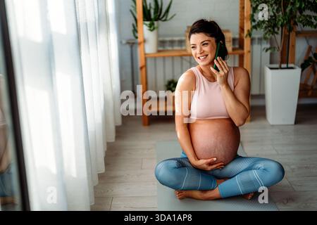 Pregnant sports woman taking a break from exercises and having phone call while relaxing at home Stock Photo