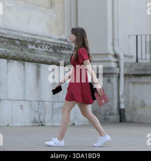 Vienna, Austria - August 26, 2022: A young woman in a red dress walks near the Karlskirche during a sunny summer day Stock Photo