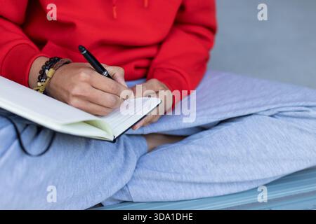 Open lined notebook lying on grey floor while black pen scribbling notes near beaded bracelets Stock Photo