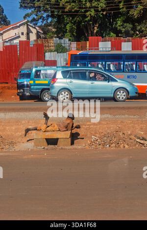 Man lying on a bench by a city road with traffic Stock Photo
