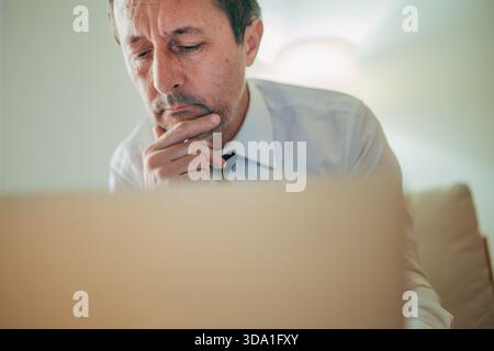 Thoughtful professional analyzing information on a laptop, focusing on strategy and decision-making. Selective focus, Stock Photo