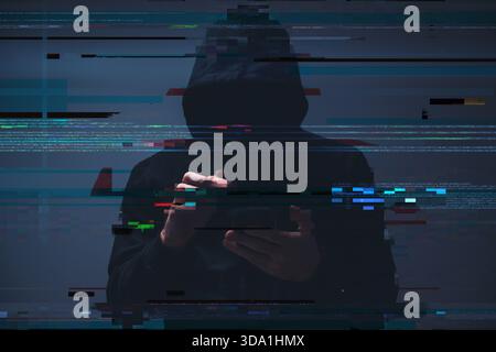 Low-key image of a hooded hacker typing on a smartphone, with digital code and glitch overlays suggesting cybercrime, data theft, and cybersecurity th Stock Photo