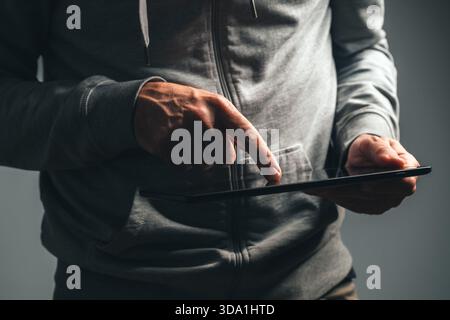 Closeup of male hands using digital tablet computer in low key light, browsing and working on touchscreen device at night. Selective focus. Stock Photo