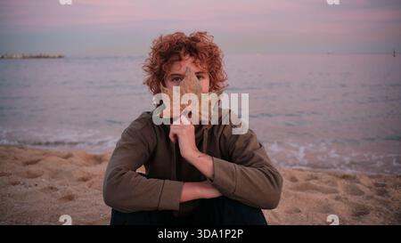 Young woman covering face with autumn leaf on beach Stock Photo