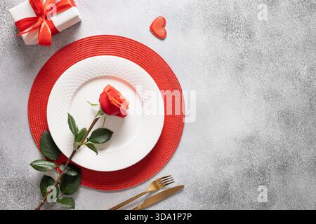 Festive table place setting with gift and red rose on gray background. View from above. Copy space. Romantic dinner for Valentine's day. Stock Photo