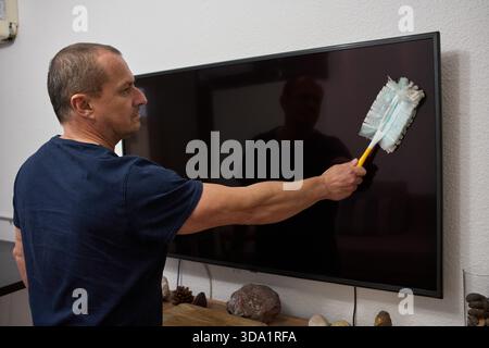 Middle-aged man cleaning television screen with microfiber duster in modern apartment living room interior Stock Photo