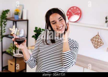 Happy pretty woman drinking red wine while singing in the kitchen at home Stock Photo