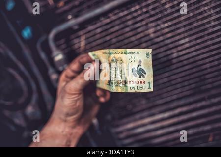 Rome, italy 20 november 2025: dirty mechanic hand holding a romanian leu banknote over a car engine. Representing working class, payments, and service Stock Photo