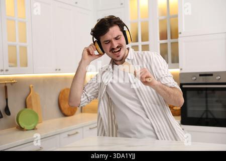Happy man in headphones with spatula singing at white marble table in kitchen Stock Photo