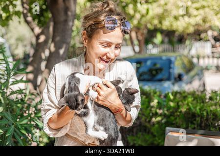 woman smiles while holding two black and white kittens Stock Photo