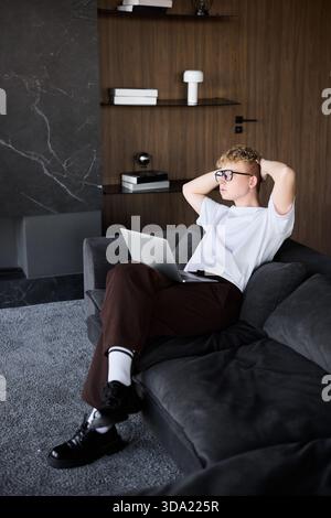 Young man relaxing on a couch while using a laptop at home Stock Photo