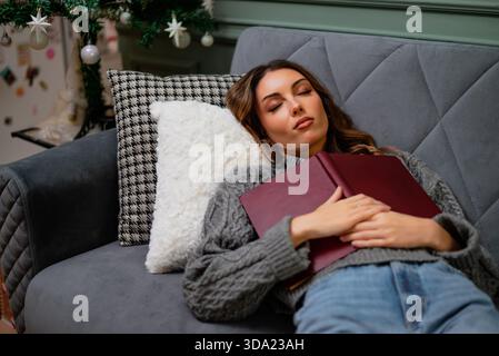 Young woman fell asleep while reading book at home. She is relaxing on her bed. Stock Photo