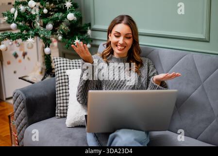 Sitting comfortably in a cozy sweater, the woman using her laptop for video call. She communicates online. Stock Photo