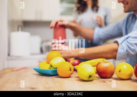 Close up of a couple using an electric juicer to make a colorful smoothie with apples, bananas and lemons. Stock Photo