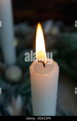 A close-up view of a single white candle burning softly in a dark, blurred background. Stock Photo