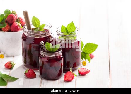 Three jars of strawberry jam with fresh strawberries on the table, close-up Stock Photo