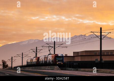 A light rail train glides beneath golden sunset skies and mountains. Stock Photo