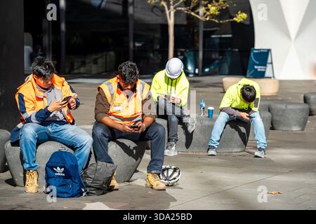 Young male construction workers in Sydney, Australia, resting and all on their mobile phones Stock Photo