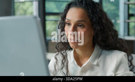 Focused Hispanic business woman working on computer in office Arabian ethnic businesswoman looking at pc monitor smiling typing browsing internet job Stock Photo