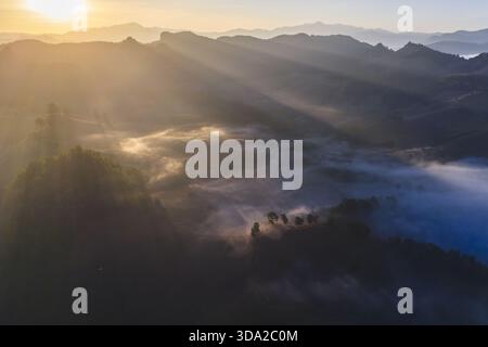 Majestic mountain landscape at sunrise, with golden sun light and rays streaming through morning fog over valley. serene and peaceful nature scene of Stock Photo