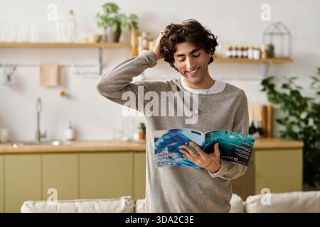 Young middle eastern man smiles while reading a magazine at his cozy apartment. Stock Photo