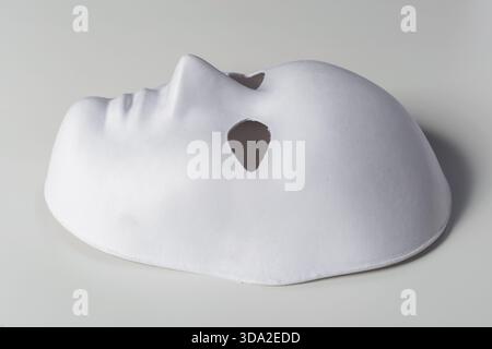 White mask resting on a flat surface with cutout eyes and nose during daylight Stock Photo