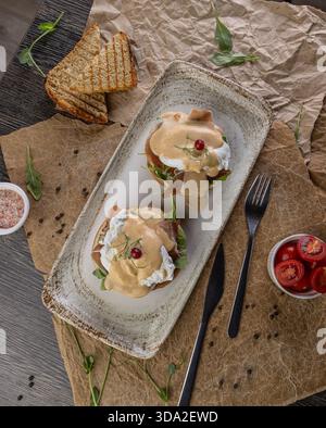 Eggs benedict with poached eggs, ham, and hollandaise sauce on a rustic plate Stock Photo