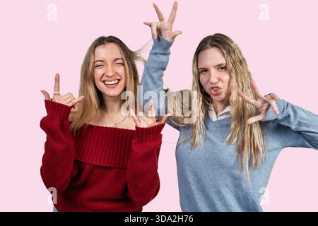 Two happy young women friends having fun posing together making peace and rock hand gestures Stock Photo