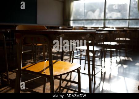 Empty Japanese Classroom with Wooden Desks, Bathed in Warm Sunlight and Dramatic Shadows Stock Photo