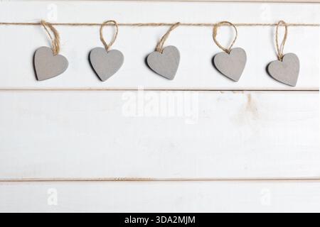 Decorative gray hearts hanging on twine against a white wooden background Stock Photo