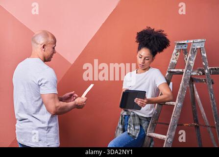 Two People Collaborating On Wall Painting With Ladder And Tablet Stock Photo