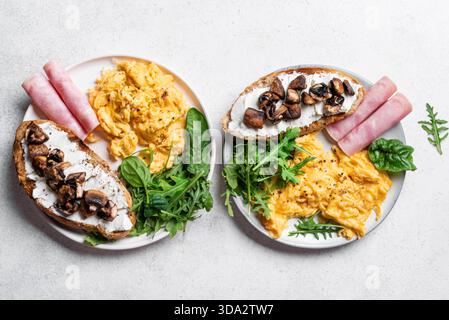 Healthy balanced breakfast plates. Scrambled eggs, greens, ham, sandwich with cream cheese and fried mushrooms. Breakfast for two, top view. Stock Photo