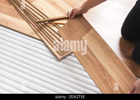 Installing laminated floor, detail on man hands holding wooden tile, over white foam base layer Stock Photo