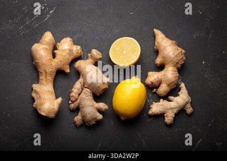 Ginger roots and whole and cut lemons creating a natural remedy concept. Healthy raw ingredients on dark textured surface Stock Photo