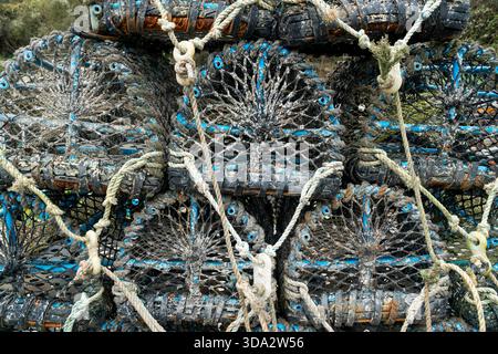 Close-up of stacked fishing pots secured with weathered ropes in harbour setting in Cornwall, showing texture, colour and coastal working detail Stock Photo