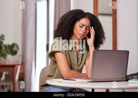 Female Worker At Home Feels Stressed While Working On Laptop At Kitchen Table Stock Photo